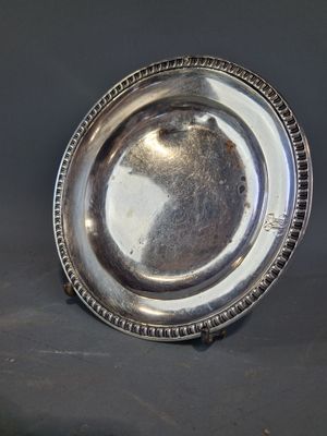un plat ancien en argent aux bords perlés posé sur une table