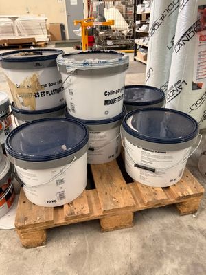 plusieurs seaux de peinture posés sur une palette dans un entrepôt