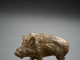 a small bronze figurine of a boar on a gray surface