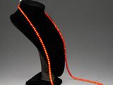 an orange beaded necklace on a mannequin stand