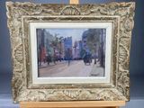 an oil painting of a street scene in a gold frame on a wooden easel