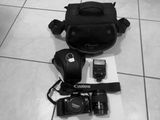photo en noir et blanc représentant un appareil photo, un sac pour appareil photo et une souris posés sur un sol carrelé