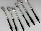 six forks and a knife are lined up on a white surface