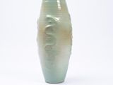 un vase vert posé sur une surface blanche
