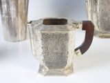 a silver coffee pot with a wooden handle next to two silver cups