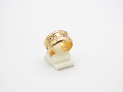 un gros plan d'une bague en or sertie de pierres roses sur un fond blanc