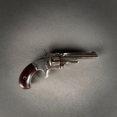 un gros plan d'un revolver posé sur une table, sur fond gris