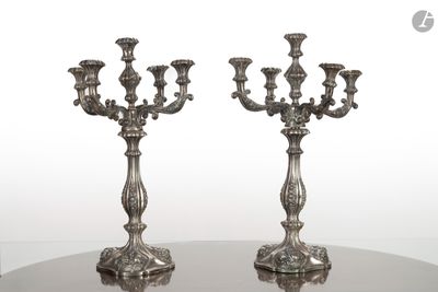 une paire de bougeoirs plaqués argent posés sur une table ronde en verre