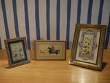 three framed pictures on a wooden table with a striped wall behind them