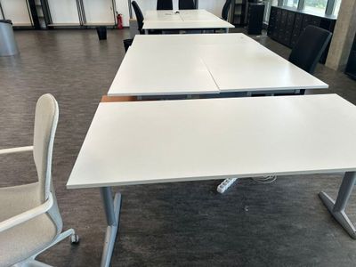 des tables et des chaises dans un bureau, sur lesquelles sont posés des écrans d'ordinateur