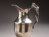 a silver pitcher sitting on a table with a dragon on it