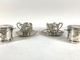 three silverplated tea cups and saucers on a white surface