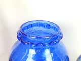 a blue glass vase sitting on a table next to a bottle