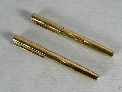 two gold colored pens sitting next to each other on a piece of paper