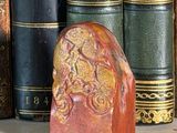 a red stone with a gold design on it in front of a row of books