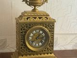 a gold clock on a wooden table with a white wall in the background