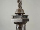 an old silver statue of a man standing on top of a tower