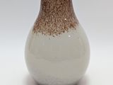 un vase blanc et marron posé sur une surface blanche