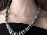 a woman wearing a necklace made of turquoise and red beads