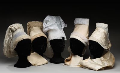 quatre mannequins coiffés de chapeaux et portant des écharpes, exposés dans une pièce sombre