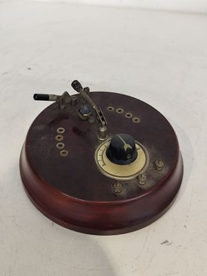 une petite horloge posée sur un socle en bois, sur une surface blanche