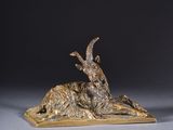 une sculpture en bronze représentant une chèvre couchée sur un socle en bois