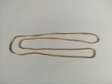 une longue chaîne en or avec un fermoir, posée sur une surface blanche