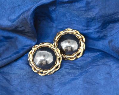 une paire de boucles d'oreilles noires et dorées posées sur un tissu bleu