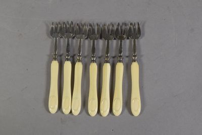 six fourchettes et un couteau sont disposés en rangée sur une surface grise