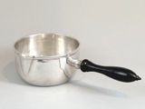 une casserole en argent avec une poignée noire posée sur une table blanche