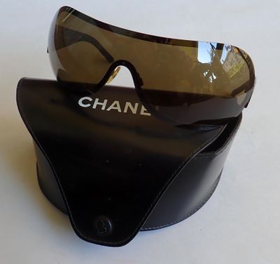 des lunettes de soleil Chanel posées sur un étui noir, sur une surface blanche