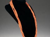 an orange beaded necklace on a black mannequin stand