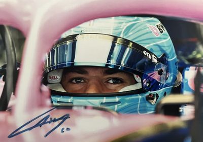 une voiture de course rose avec un homme casqué assis au volant