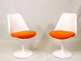 une paire de chaises « Tulip » blanches avec des coussins orange sur fond blanc