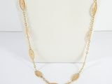 a gold necklace with a long chain that has a leaf design on it