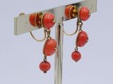 pair of red coral and gold earrings on a silver stand