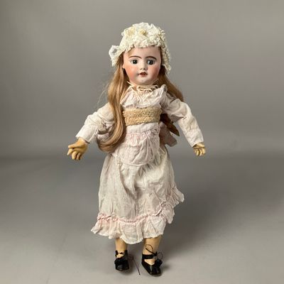 une poupée ancienne en porcelaine représentant une femme vêtue d'une robe blanche et d'un chapeau