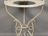 une table en fer forgé blanc avec un plateau en verre et un piètement en métal