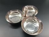 three silver plated dishes on a black table with a silver figurine in the middle