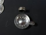 a silver object on a black table next to a coin