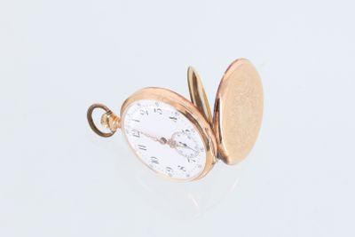 une petite montre de poche en or posée sur une surface blanche