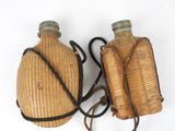pair of antique wicker water bottles with leather straps on white background