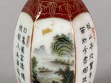 a red vase with a painting on it sitting on a table