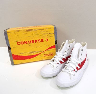 une paire de Converse rouges et blanches posée à côté d'un carton de Coca-Cola