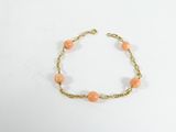 un bracelet en chaîne dorée orné de perles orange sur fond blanc