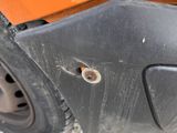the rear end of an orange car with a hole in it ' s bumper