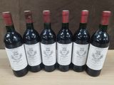 six bottles of red wine lined up on a wooden table