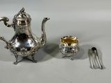 a silver tea pot and a silver spoon on a white table