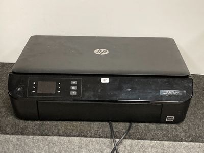 L'imprimante HP est posée sur la moquette, près du mur.