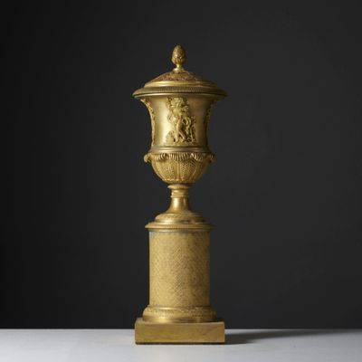 un vase doré posé sur une table blanche, près d'un mur noir